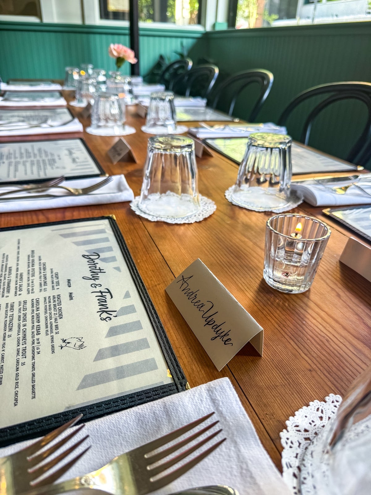 A set dining table at a restaurant with menus, napkins, cutlery, glasses upside down, a small candle, and a name card reading "Amelia Vaughan"&mdash;perfect for those exploring Things to Do in Roanoke VA.