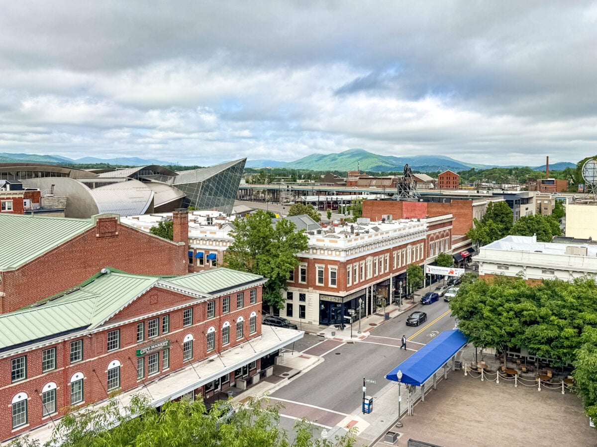 Aerial view of downtown Roanoke, VA with red brick buildings, tree-lined streets, and green hills&mdash;offering a scenic backdrop for discovering the many things to do in Roanoke VA under a partly cloudy sky.