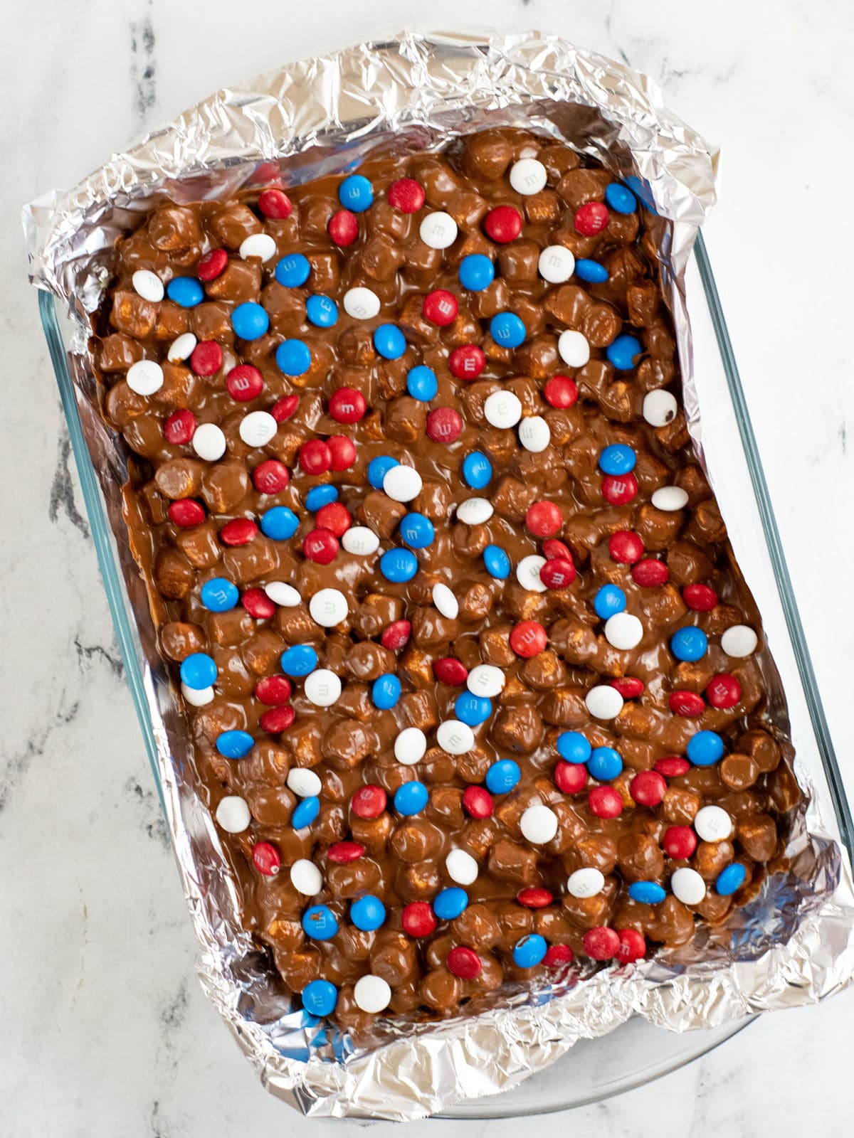 A rectangular baking dish lined with foil contains chocolate dessert topped with red, white, and blue candy-coated chocolates.