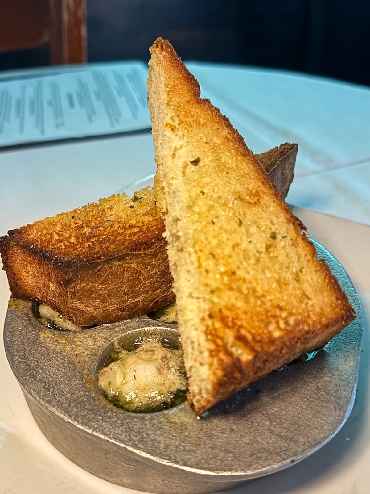 Three pieces of toasted bread are placed on a dish with baked escargot in compartments filled with herb butter.