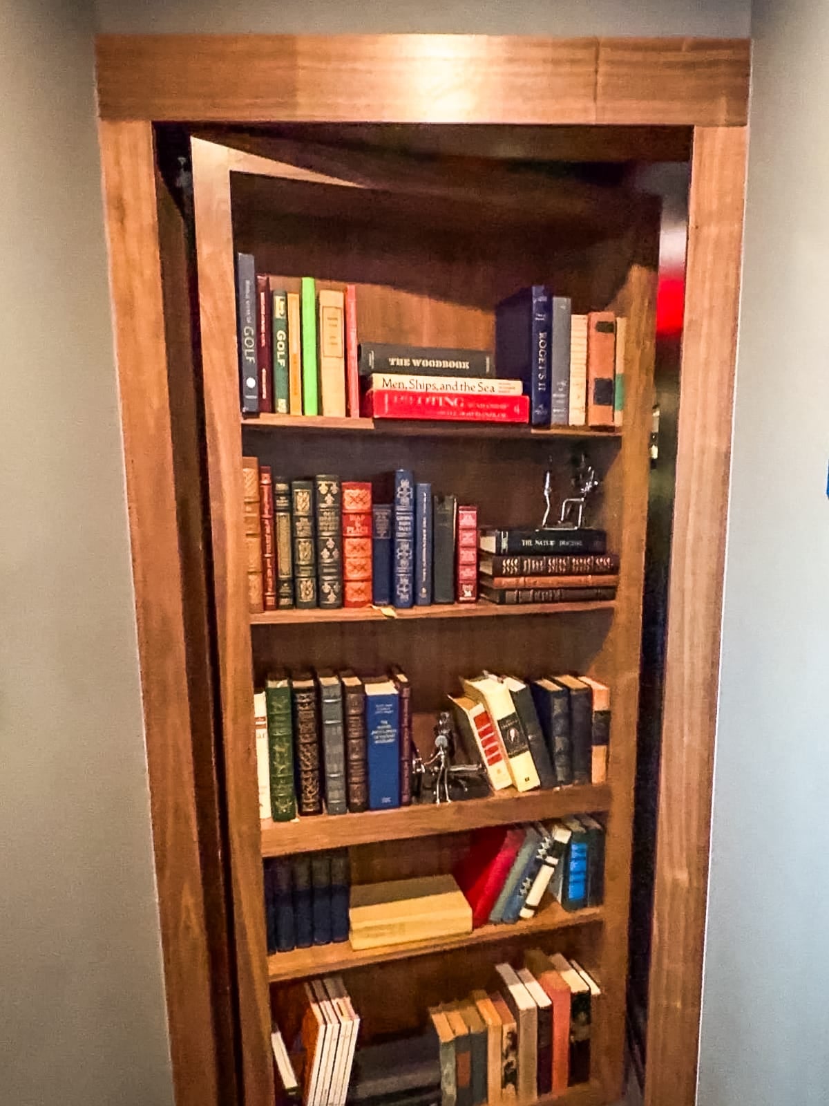 A wooden bookshelf filled with books partially opens to reveal itself as a hidden door in a wall.